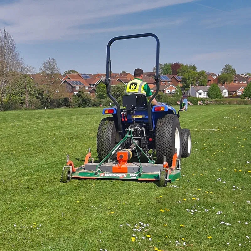 Tractor mowing a grassy field with houses in the background