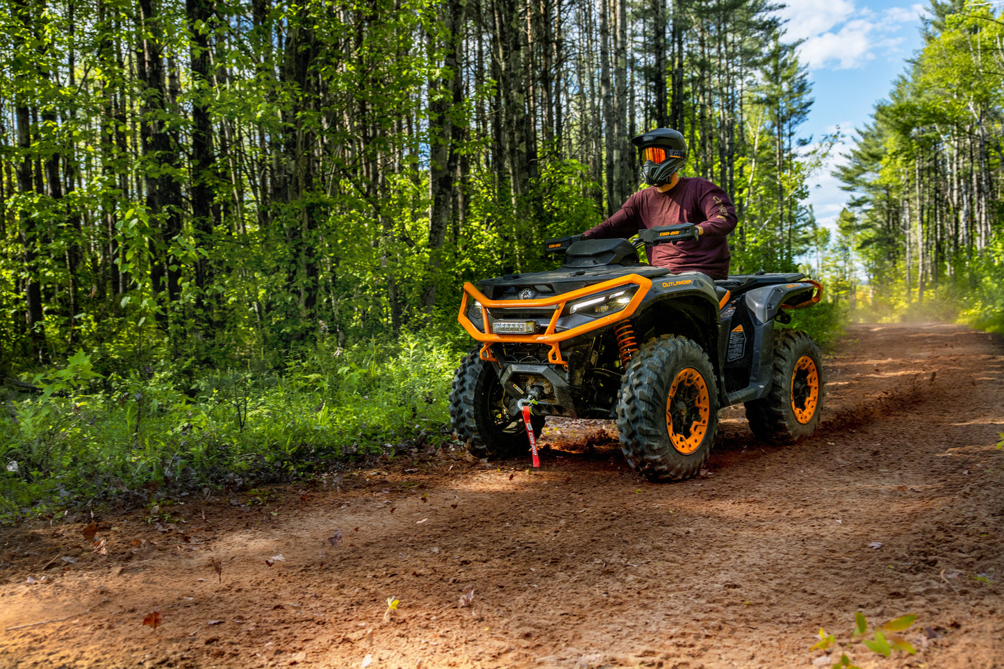 Person riding a Can-Am Outlander ATV on a dirt trail through a forest