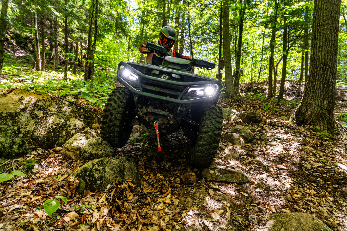 Person riding a Can-Am Outlander ATV through a forest on a sunny day