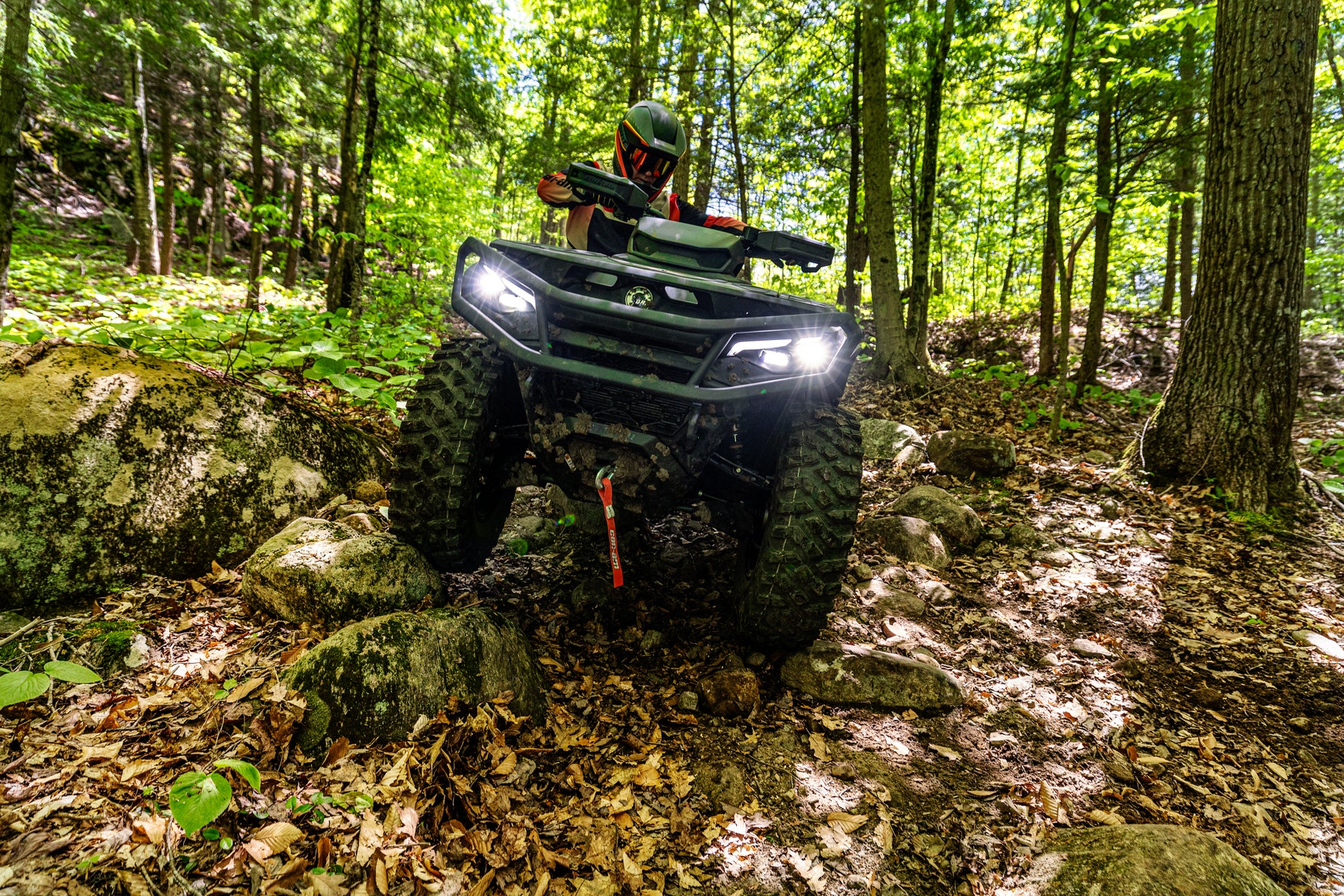 Person riding a Can-Am Outlander ATV through a forest on a sunny day