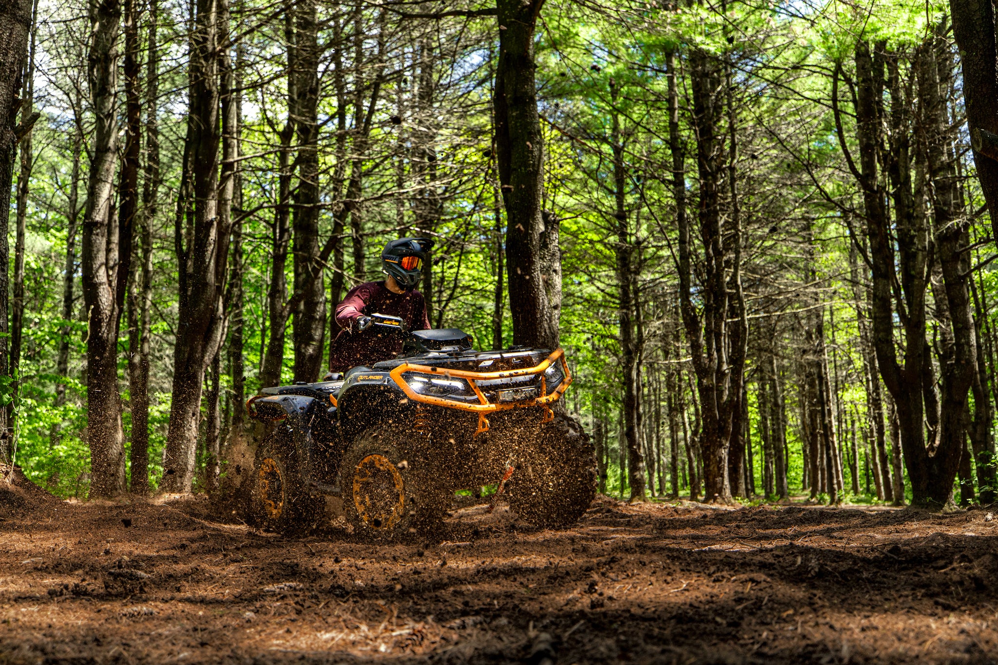 Person riding a Can-Am Outlander ATV through a forest