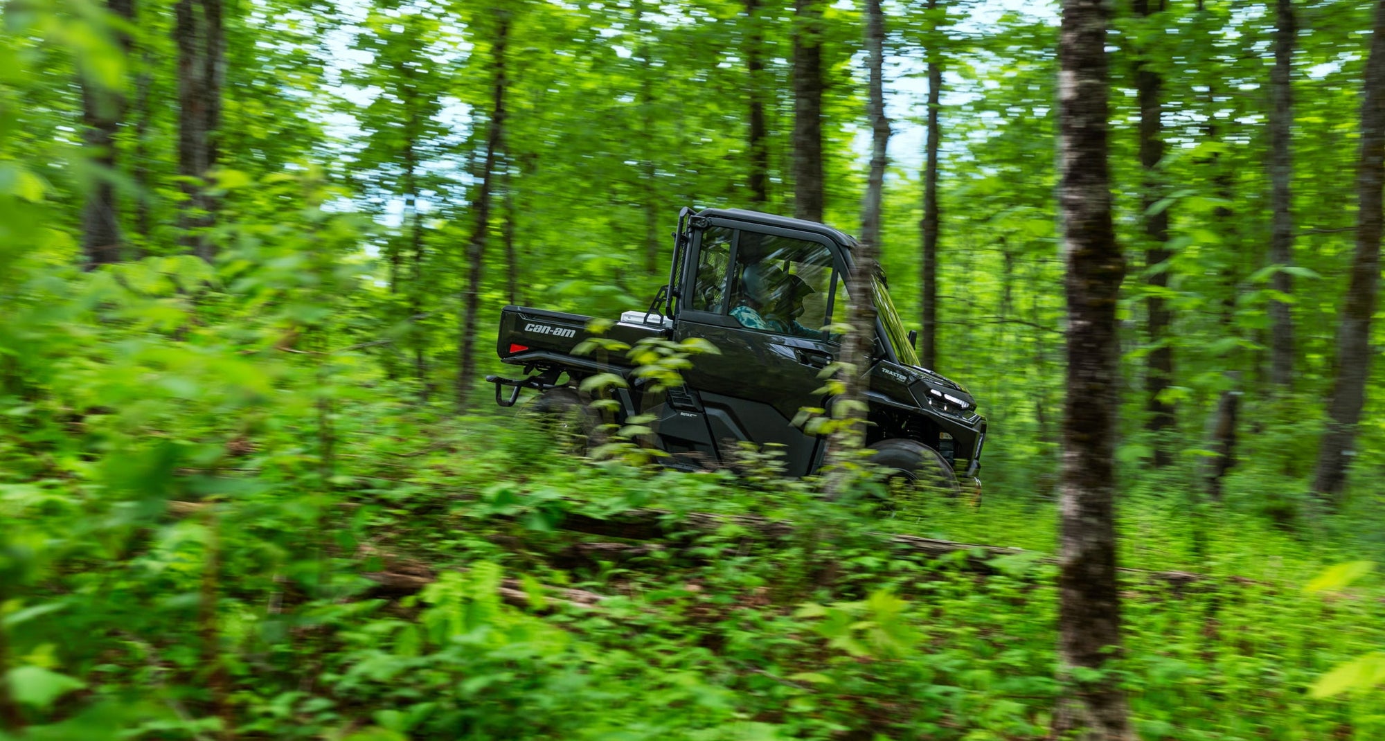 Black Can-Am utility vehicle driving through a dense forest