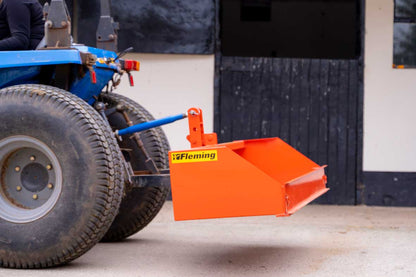 Fleming tractor transport box attached to a blue tractor with a building in the background