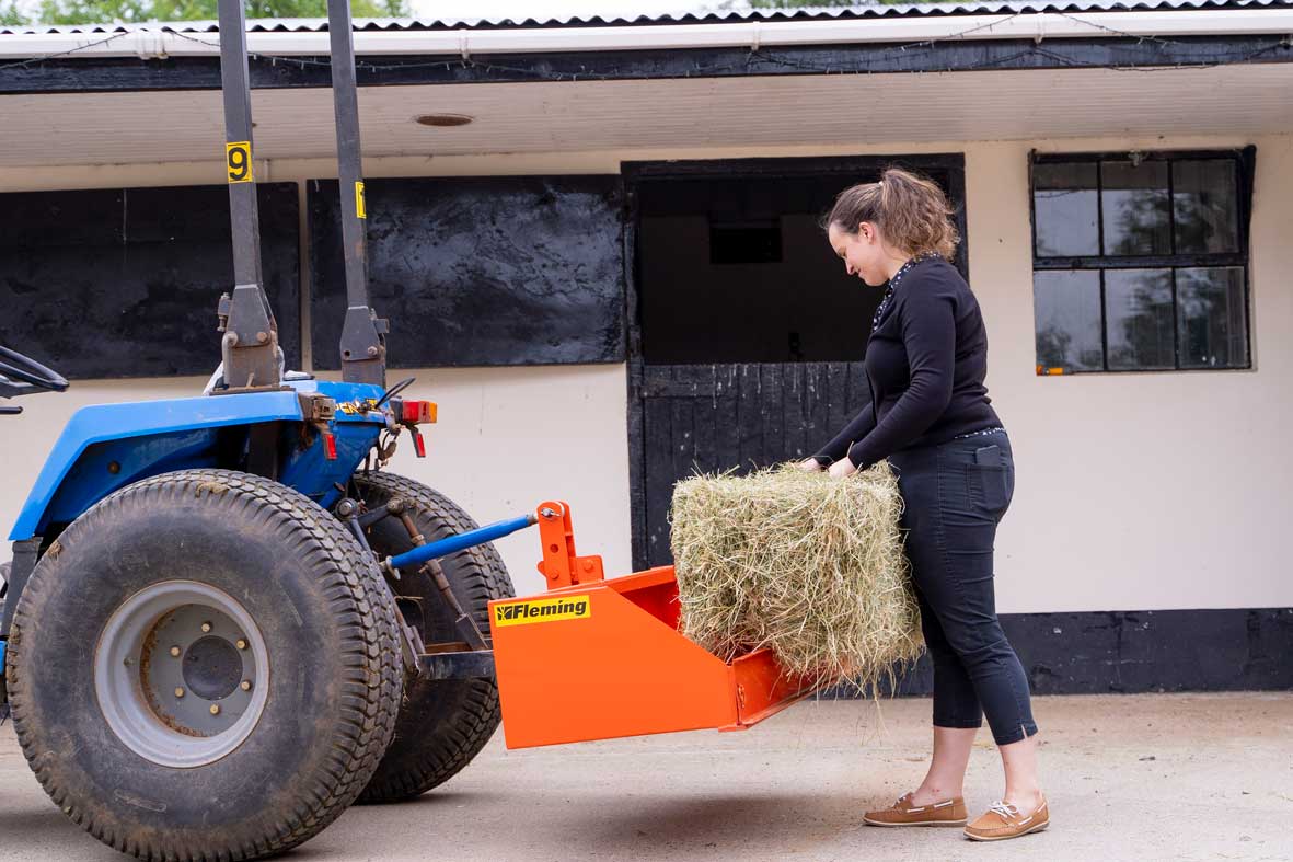 Person loading hay into a Fleming tractor transport box