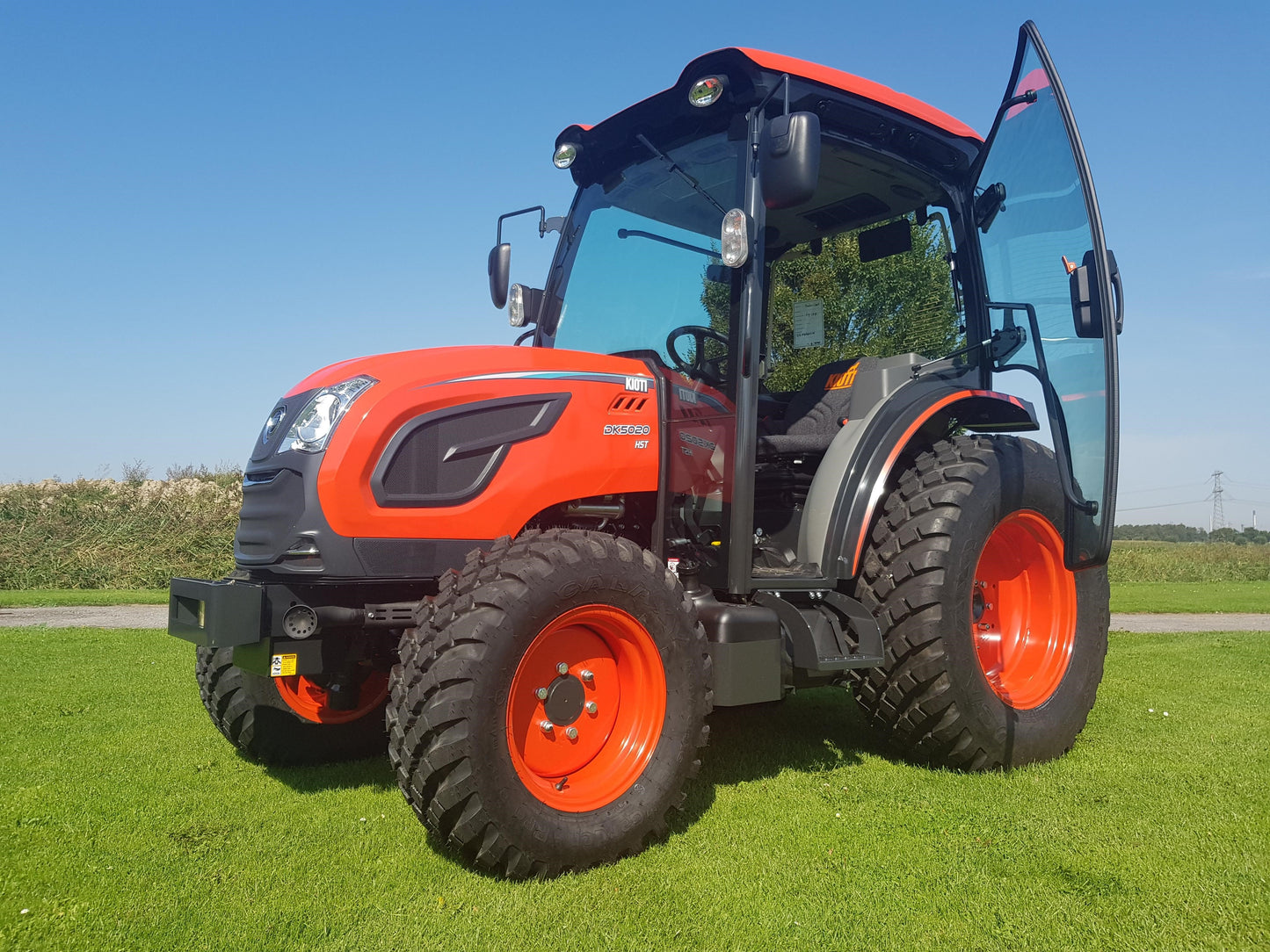 Kioti tractor on a grassy field with a clear blue sky.