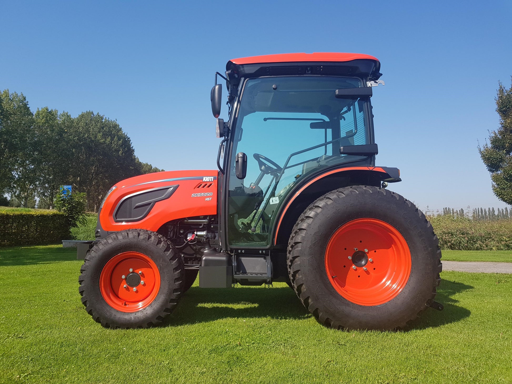 Kioti tractor on a grassy field with trees in the background