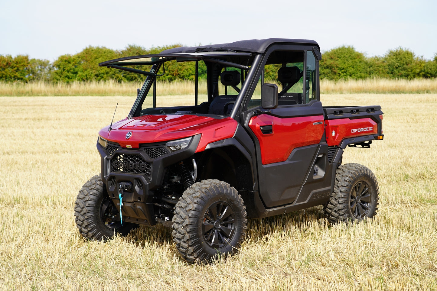 Red CFMOTO off-road vehicle in a field with trees in the background