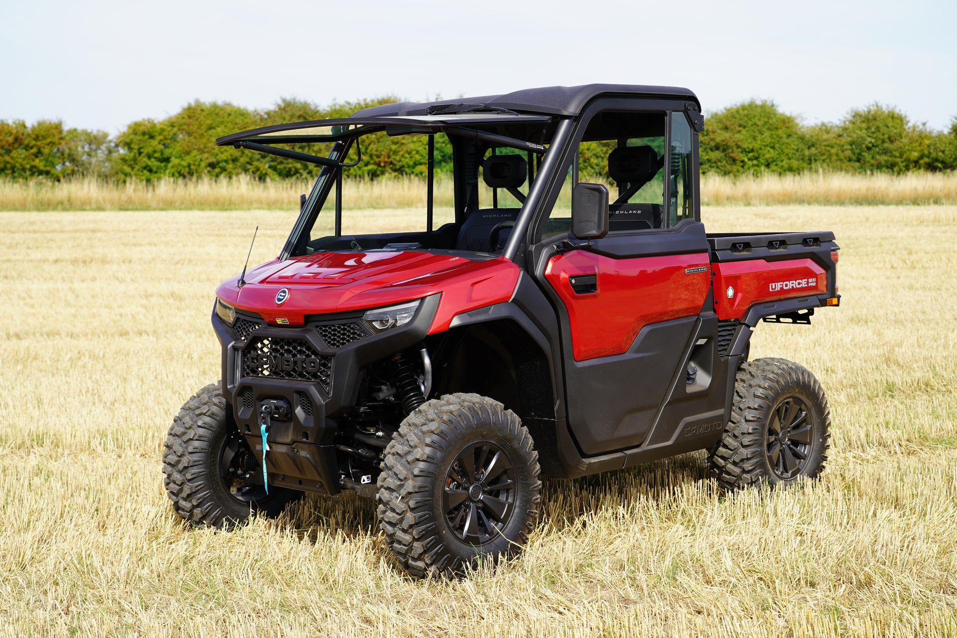 Red CFMOTO off-road vehicle in a field with trees in the background