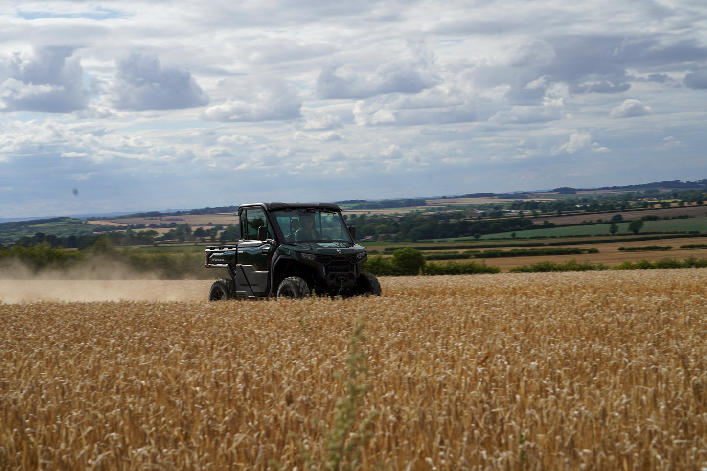 CFMOTO U10 Pro utility vehicle driving through a wheat field with a cloudy sky.