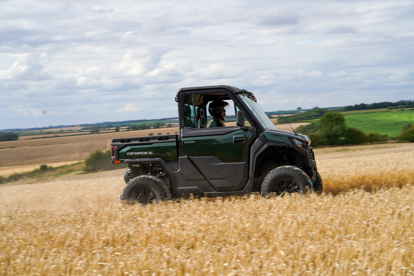 Green CFMOTO U10 Pro utility vehicle driving through a wheat field with a scenic background