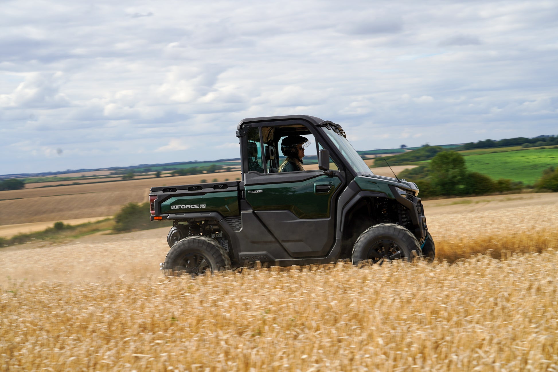 Green CFMOTO U10 Pro utility vehicle driving through a wheat field with a scenic background