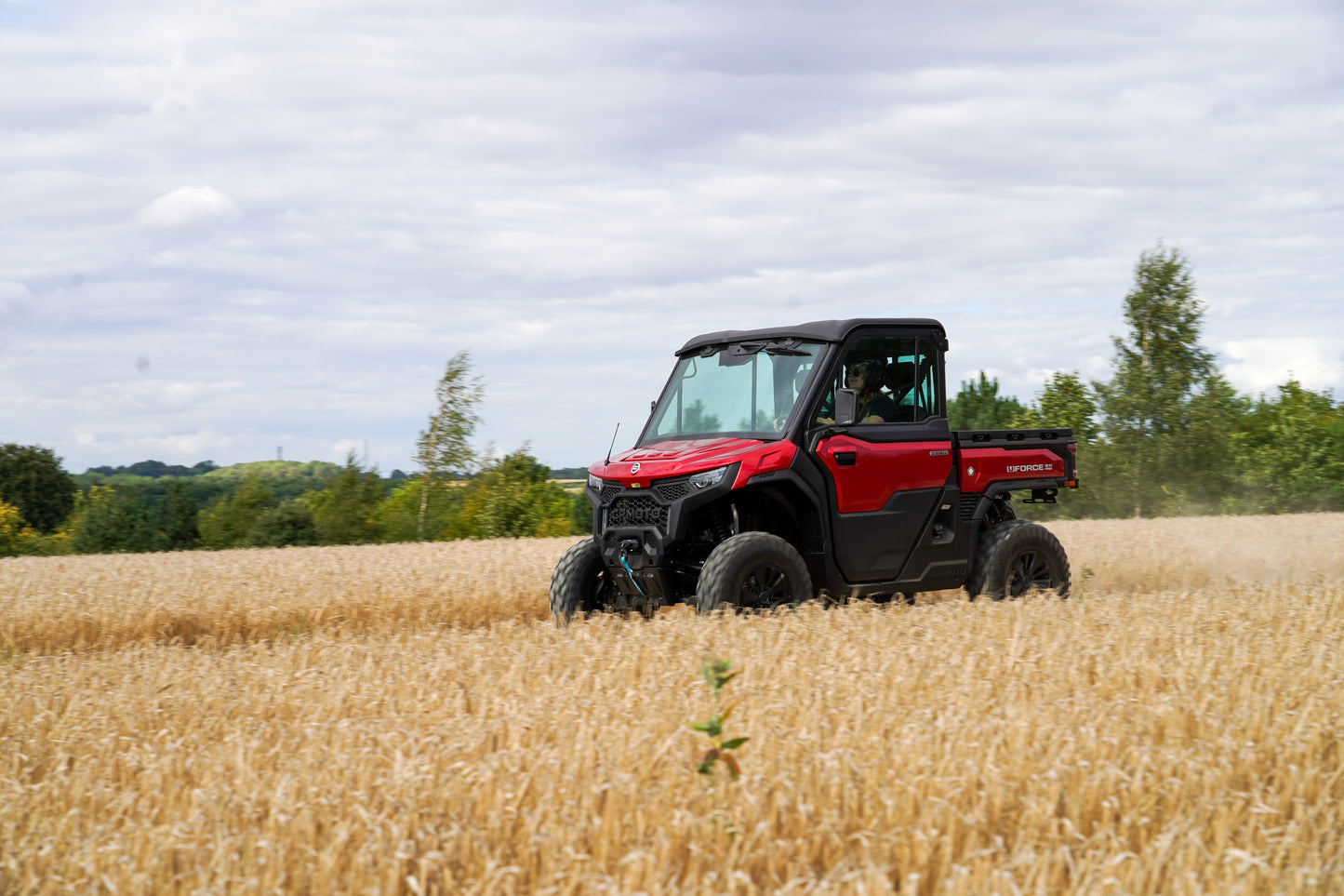 Red CFMOTO U10 Pro utility vehicle in a field with trees and sky in the background