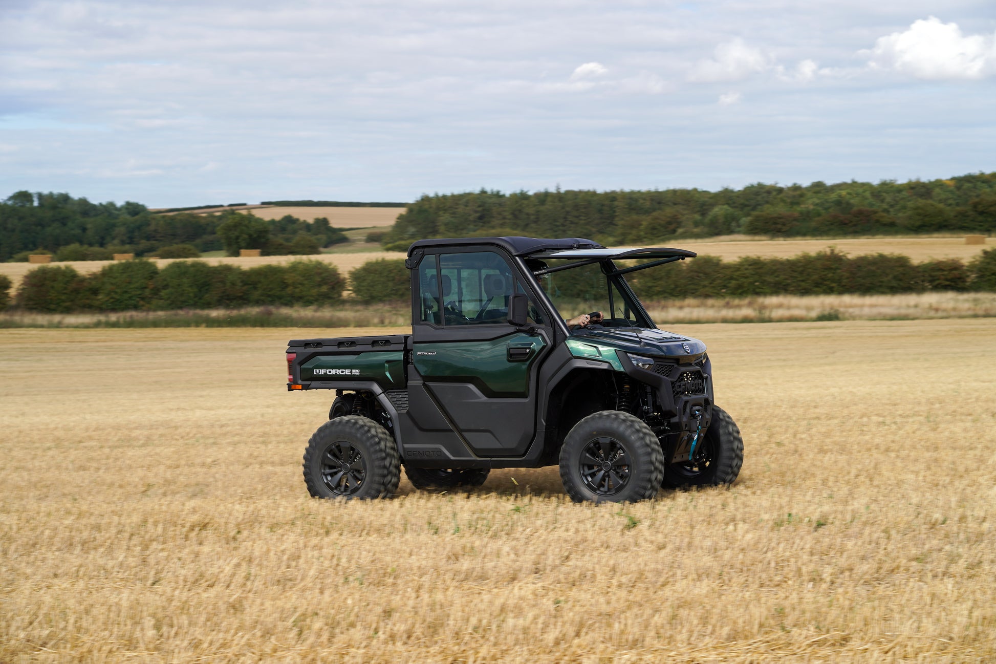 Green CFMOTO U10 Pro utility vehicle in a field with a rural landscape in the background