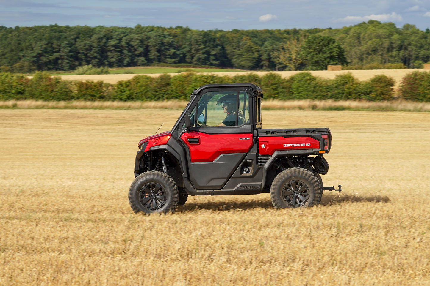 Red CFMOTO UTV in a field with trees in the background
