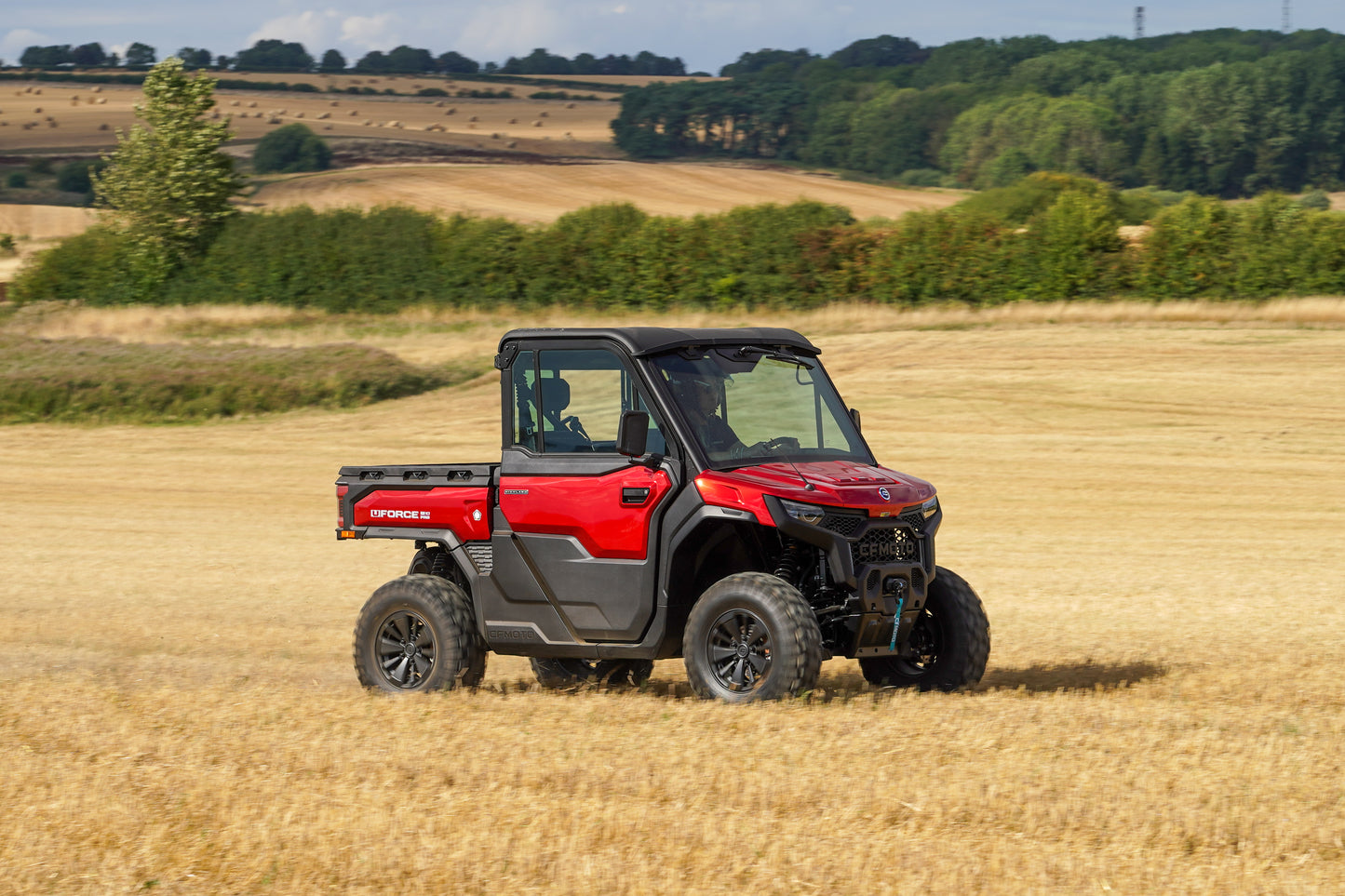 Red CFMOTO UTV in a field with a rural landscape in the background