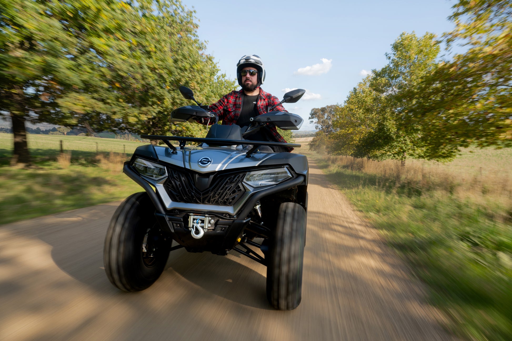 Person riding a CFMOTO ATV on a dirt road with trees in the background