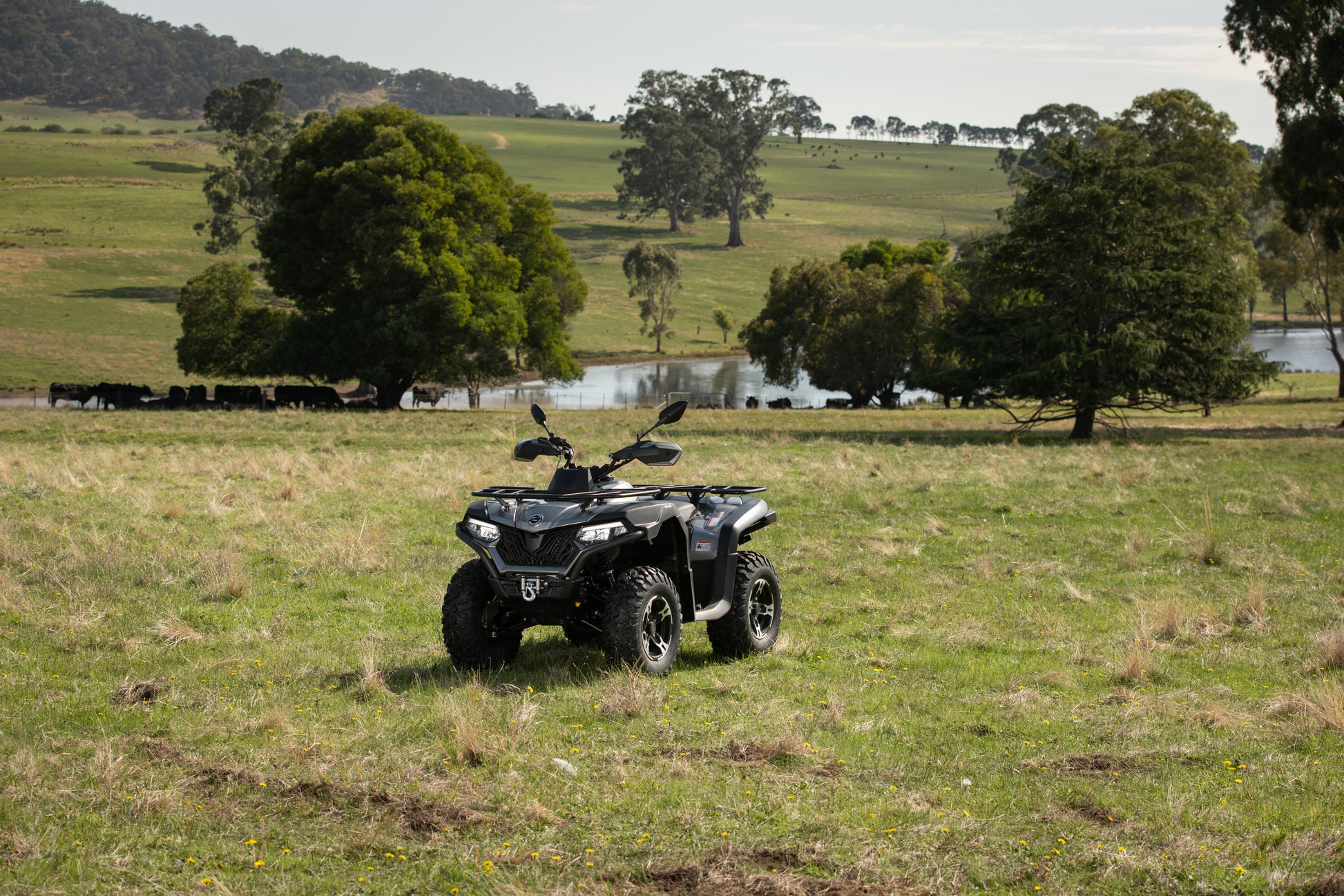 CFMOTO ATV in a grassy field with trees and a lake in the background