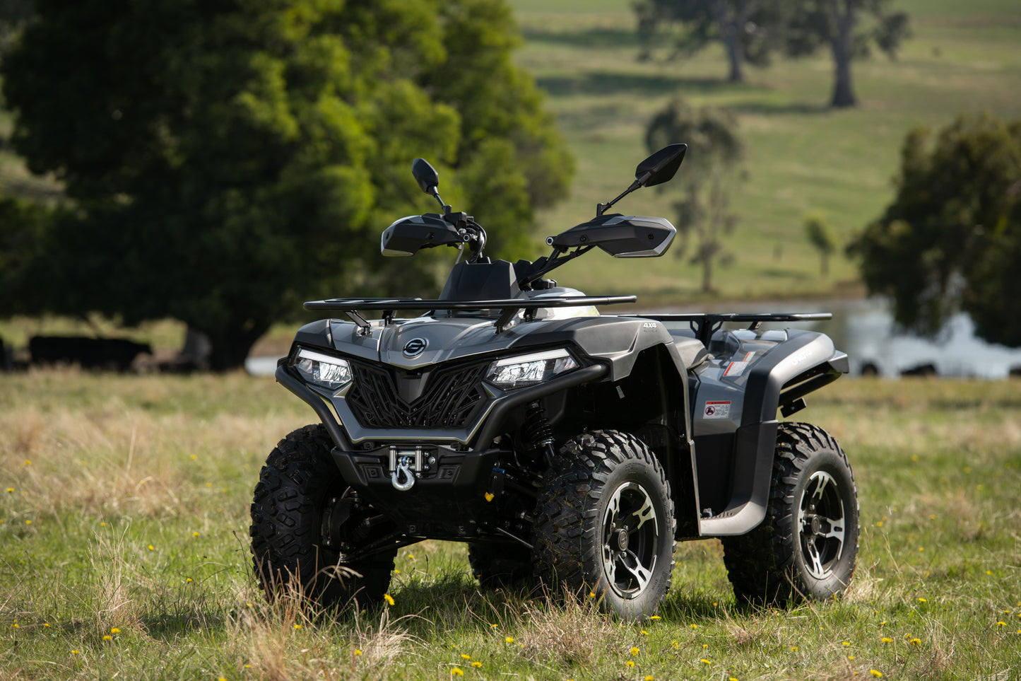 CFMOTO quad bike parked in a grassy field with trees in the background