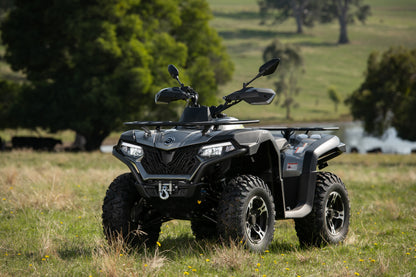 CFMOTO quad bike parked in a grassy field with trees in the background