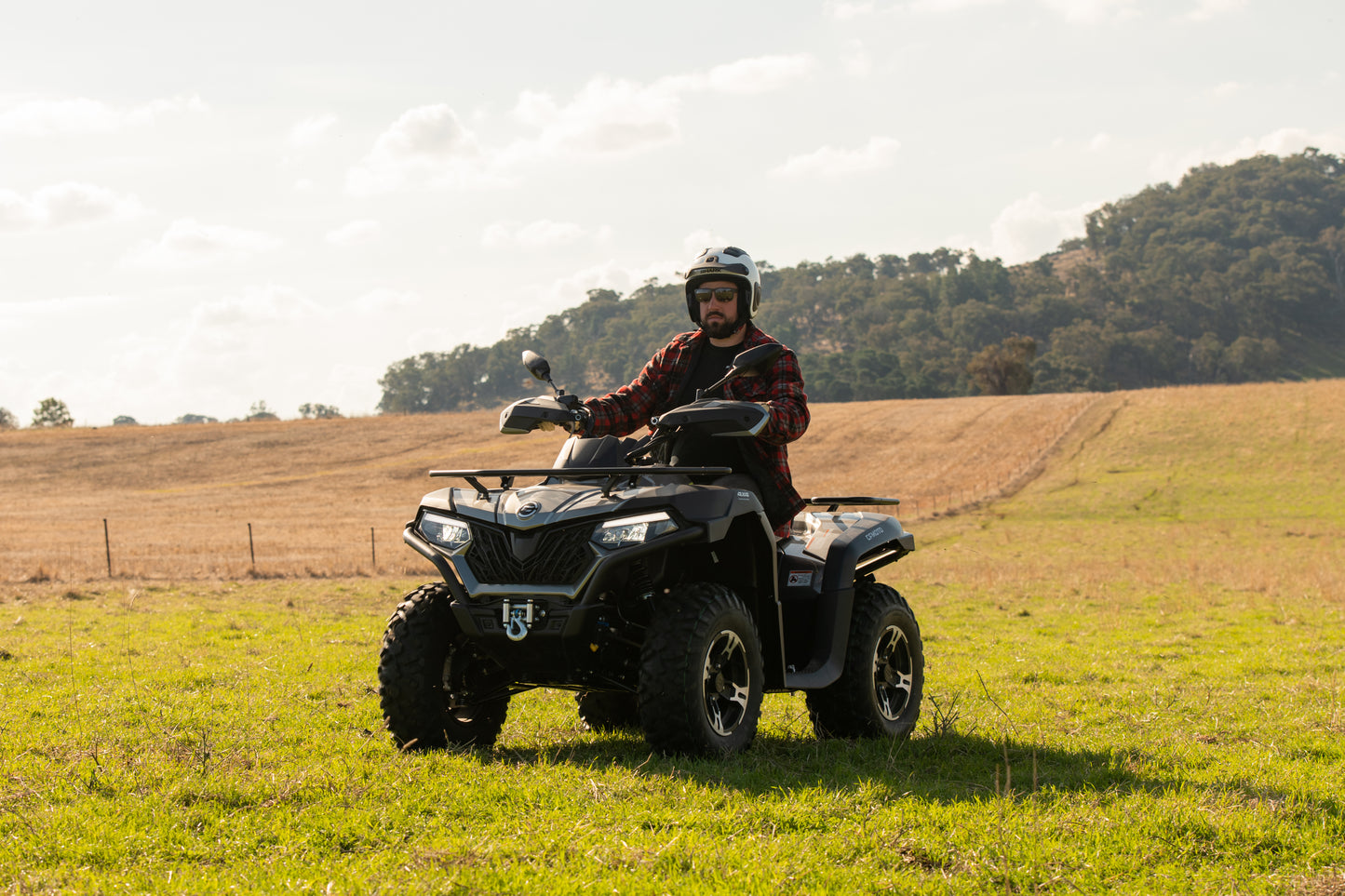 Person riding a CFMOTO quad bike in a grassy field with trees in the background