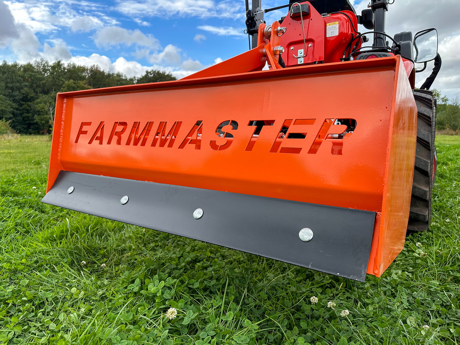 FarmMaster tractor box grader on a grassy field with a blue sky.