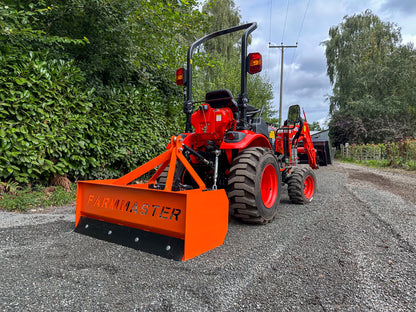 FarmMaster tractor box grader attachment on a gravel road surrounded by trees.
