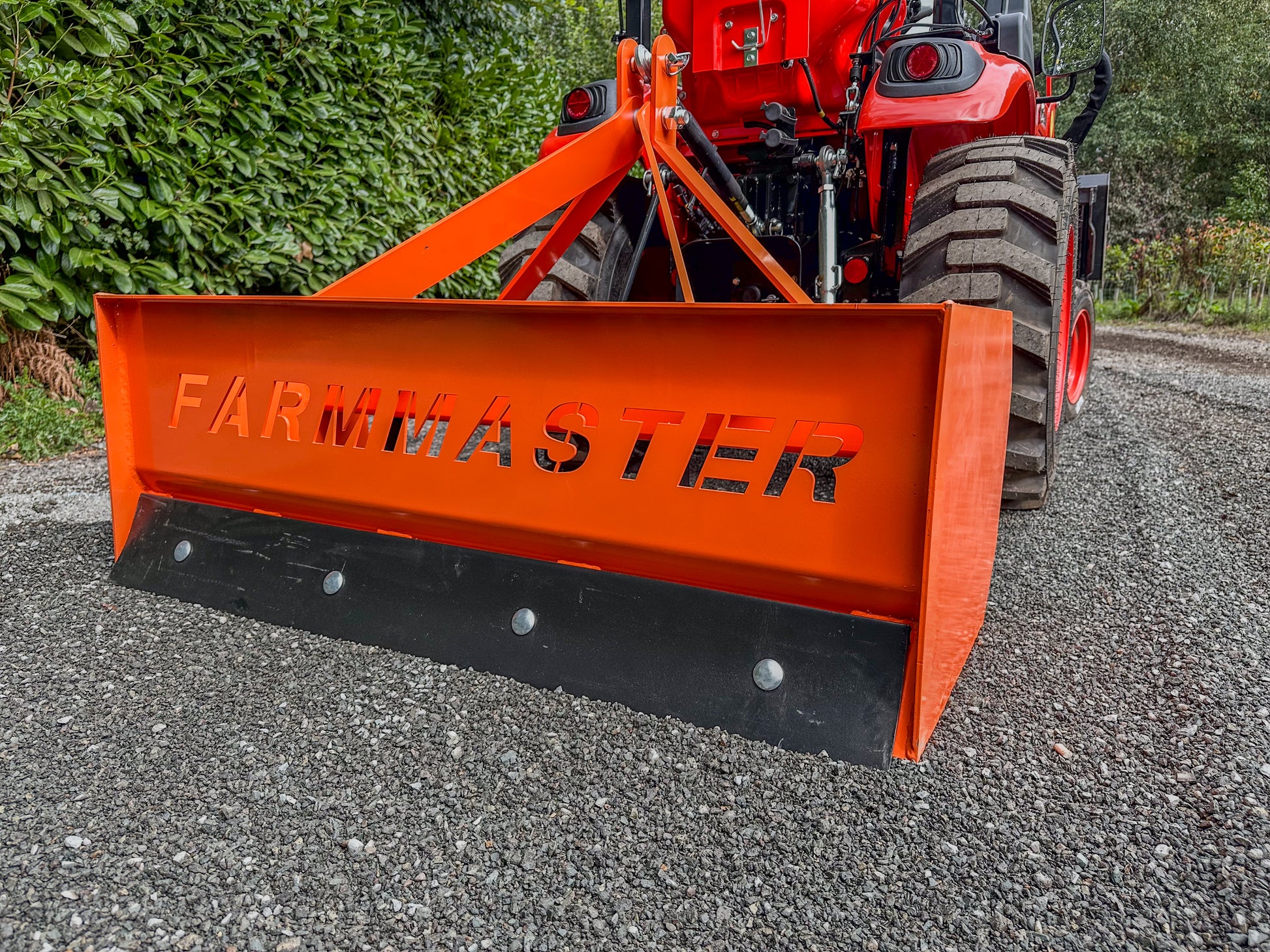 FarmMaster tractor box grader attachment on a gravel road with greenery in the background