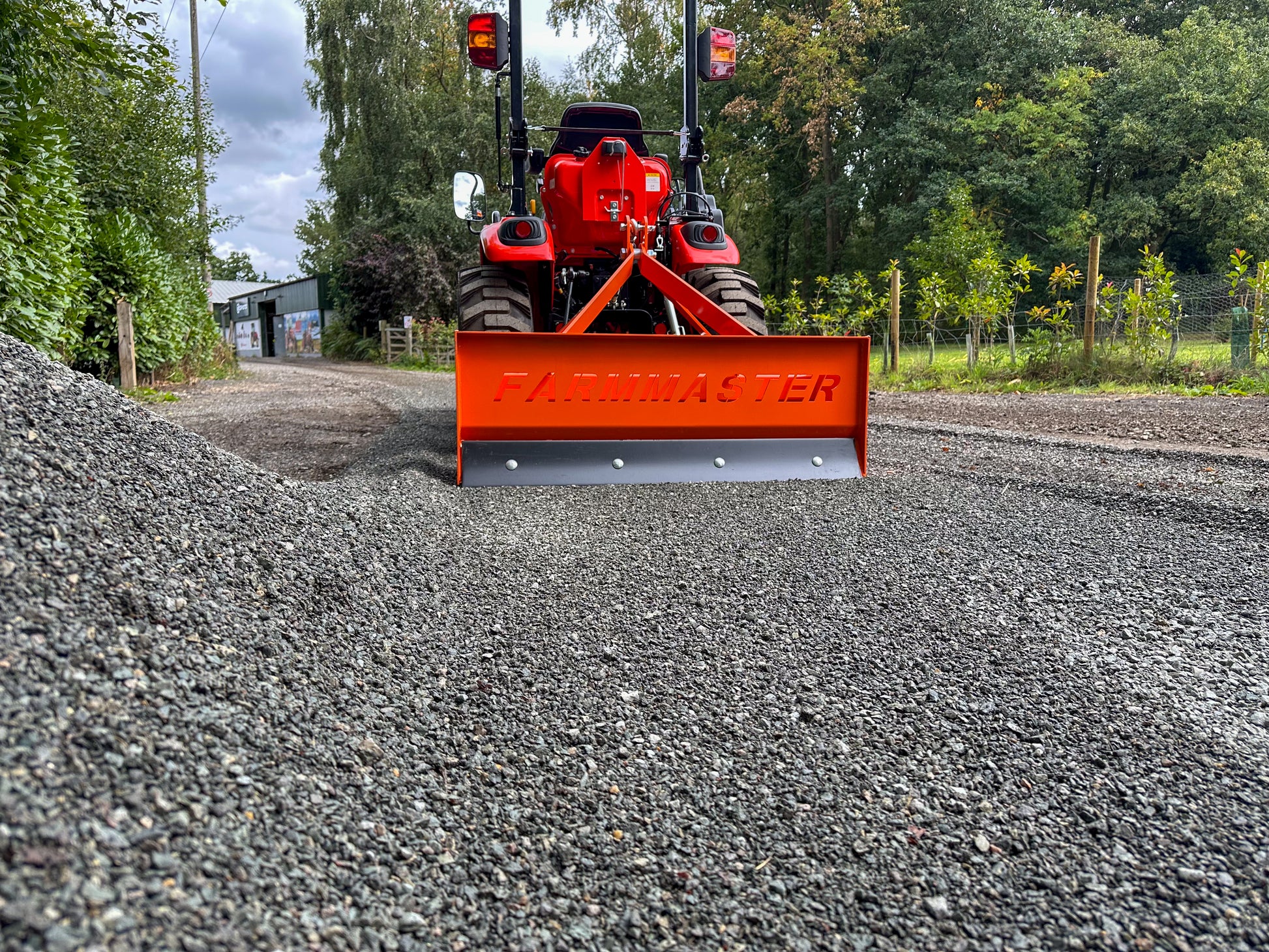 FarmMaster tractor box grader attachment on a gravel road with trees in the background