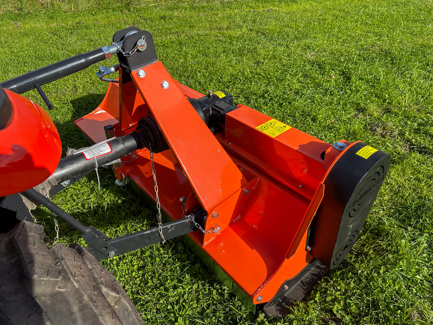 Close-up of a red agricultural tractor with a FarmMaster flail mower on a grassy field