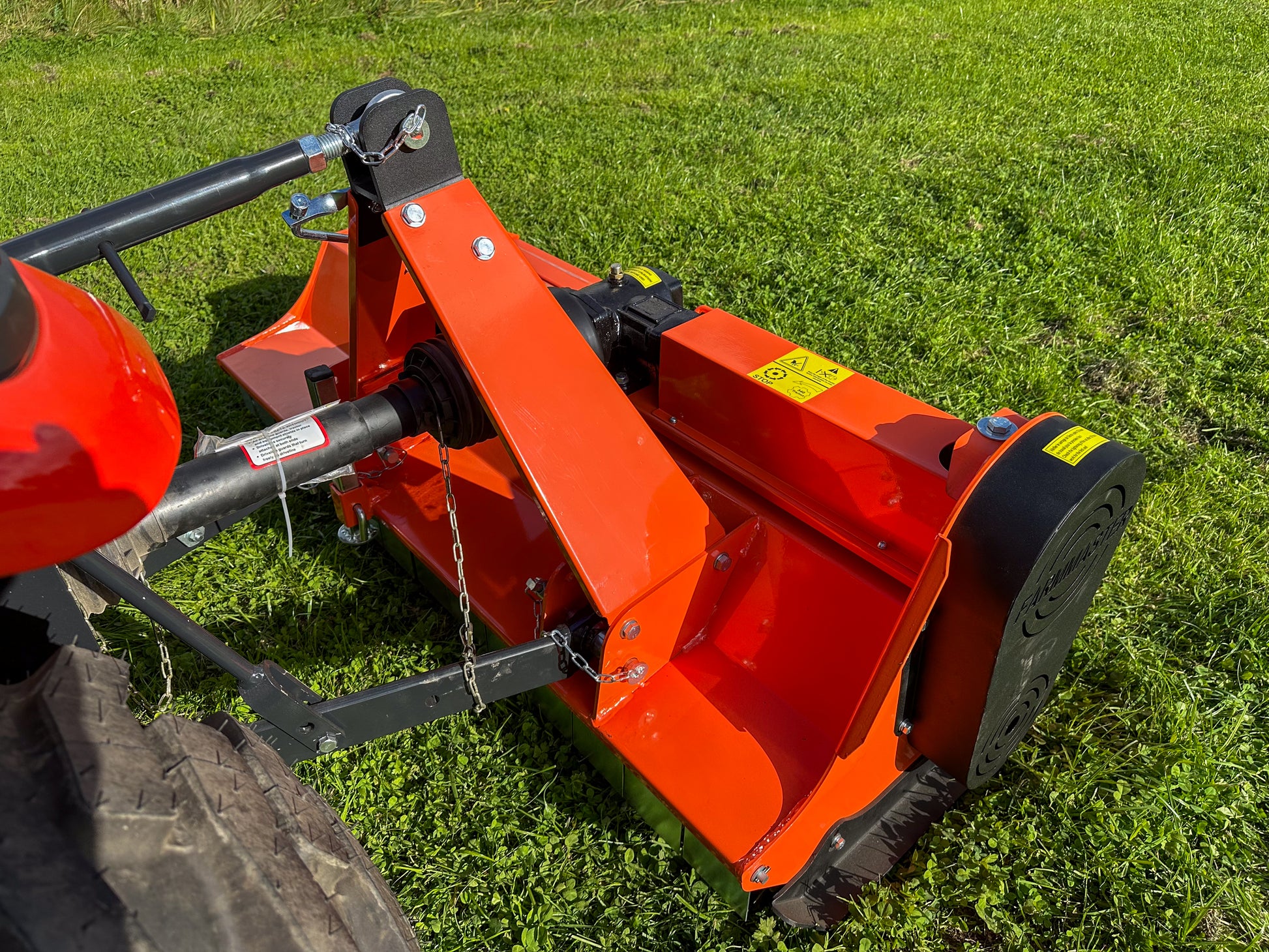 Close-up of a red agricultural tractor with a FarmMaster flail mower on a grassy field