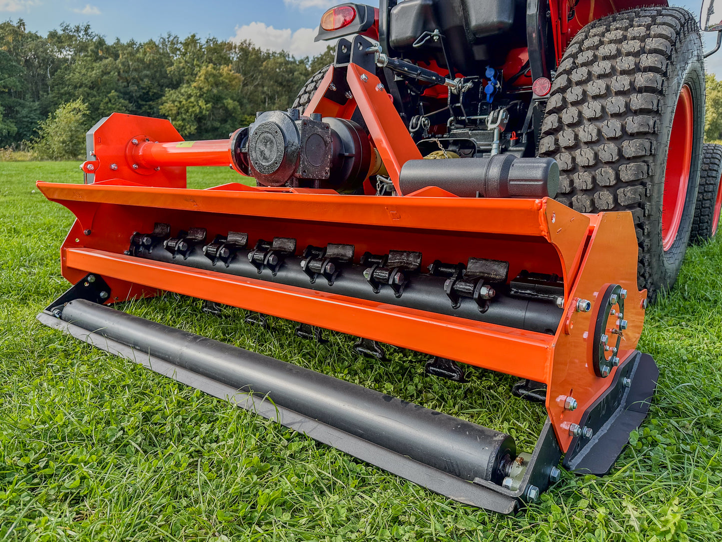 Close-up of a FarmMaster tractor flail mower on grass with trees in the background