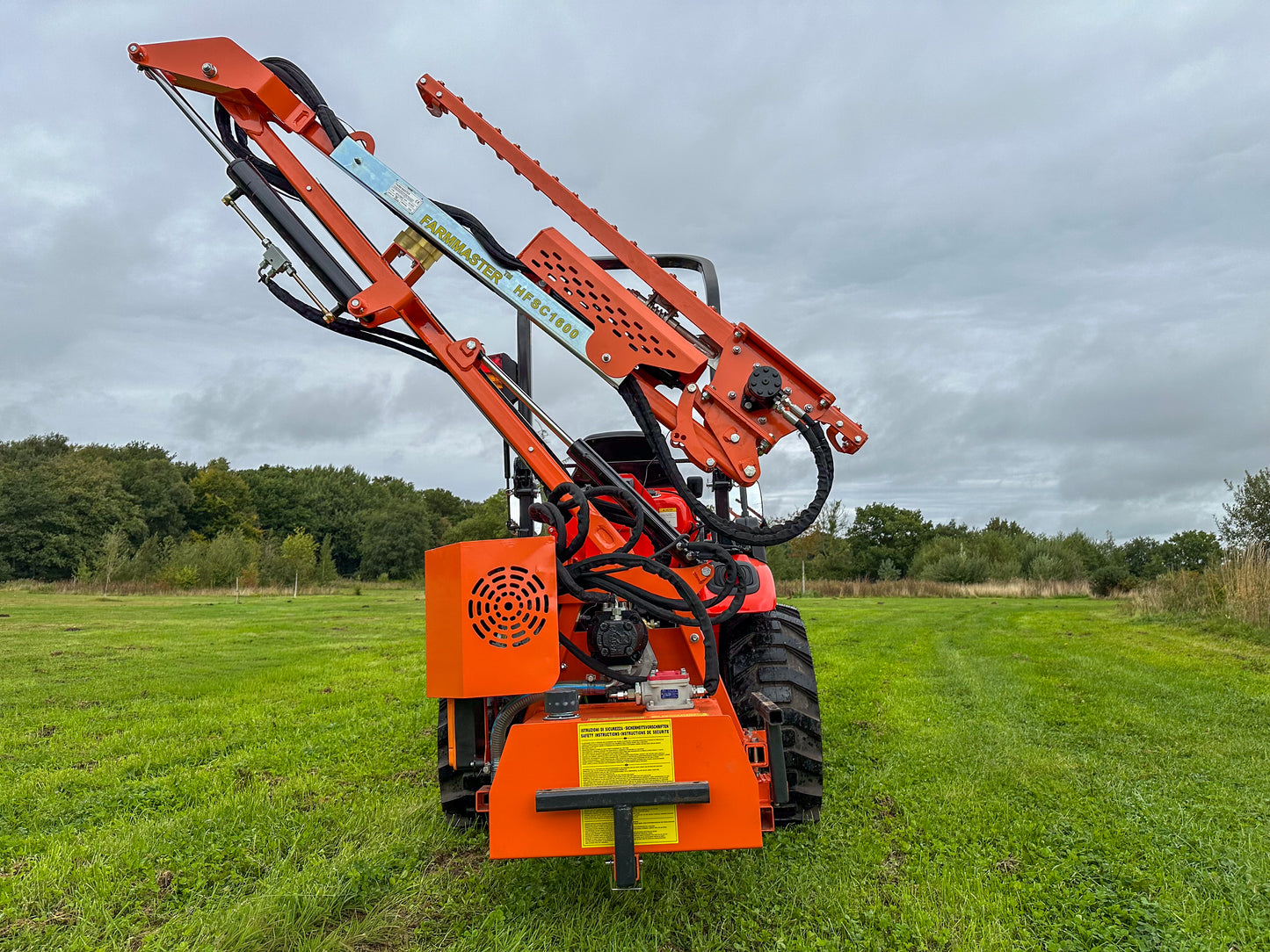 FarmMaster tractor hedge cutter on a grassy field with trees in the background