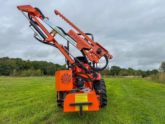 FarmMaster tractor hedge cutter on a grassy field with trees in the background