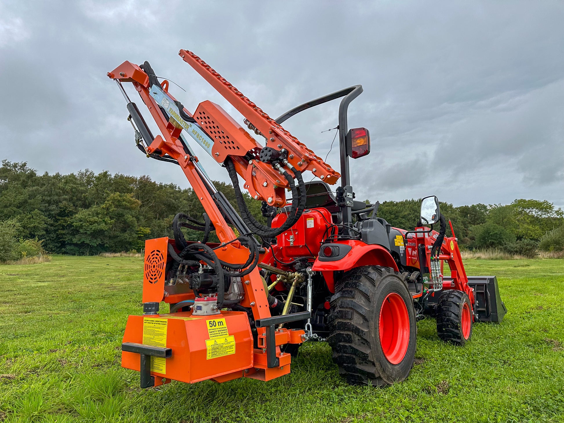 Kioti tractor with a large hedge cutter attachment in a grassy field