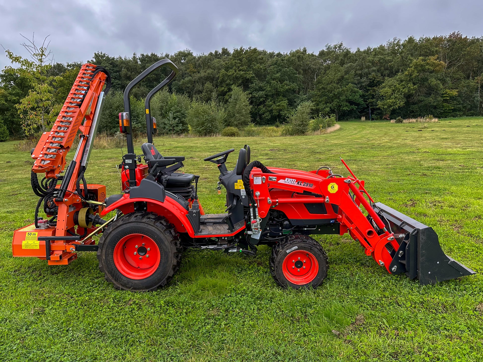 Kioti tractor with FarmMaster tractor hedge cutter on a grassy field with trees in the background