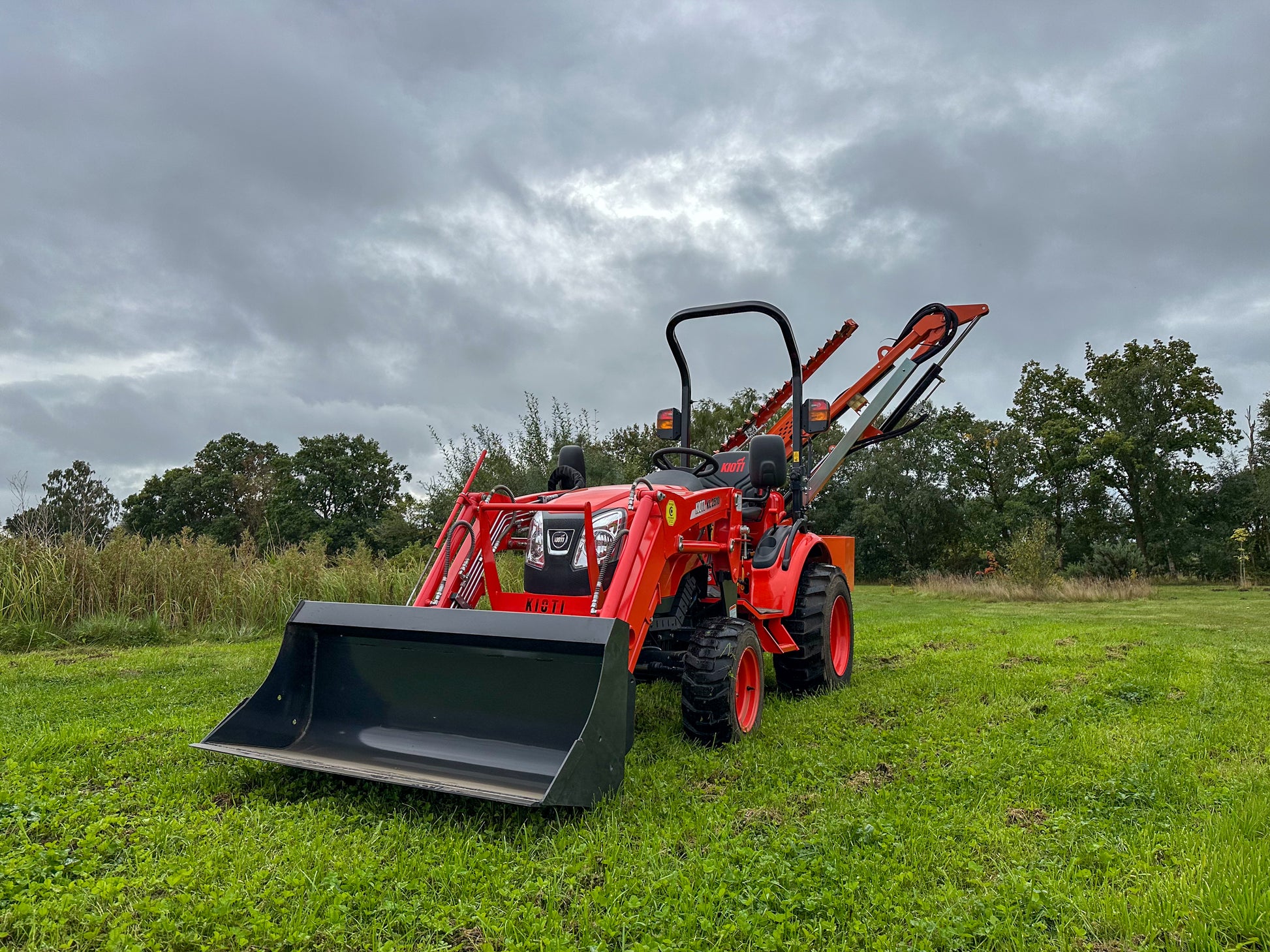 FarmMaster tractor hedge cutter in a grassy field under a cloudy sky