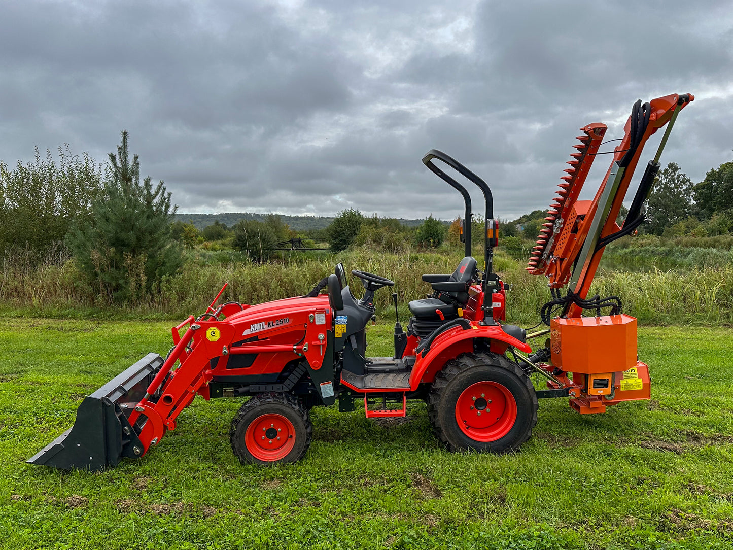 Kioti tractor with FarmMaster attachment in a grassy field on a cloudy day