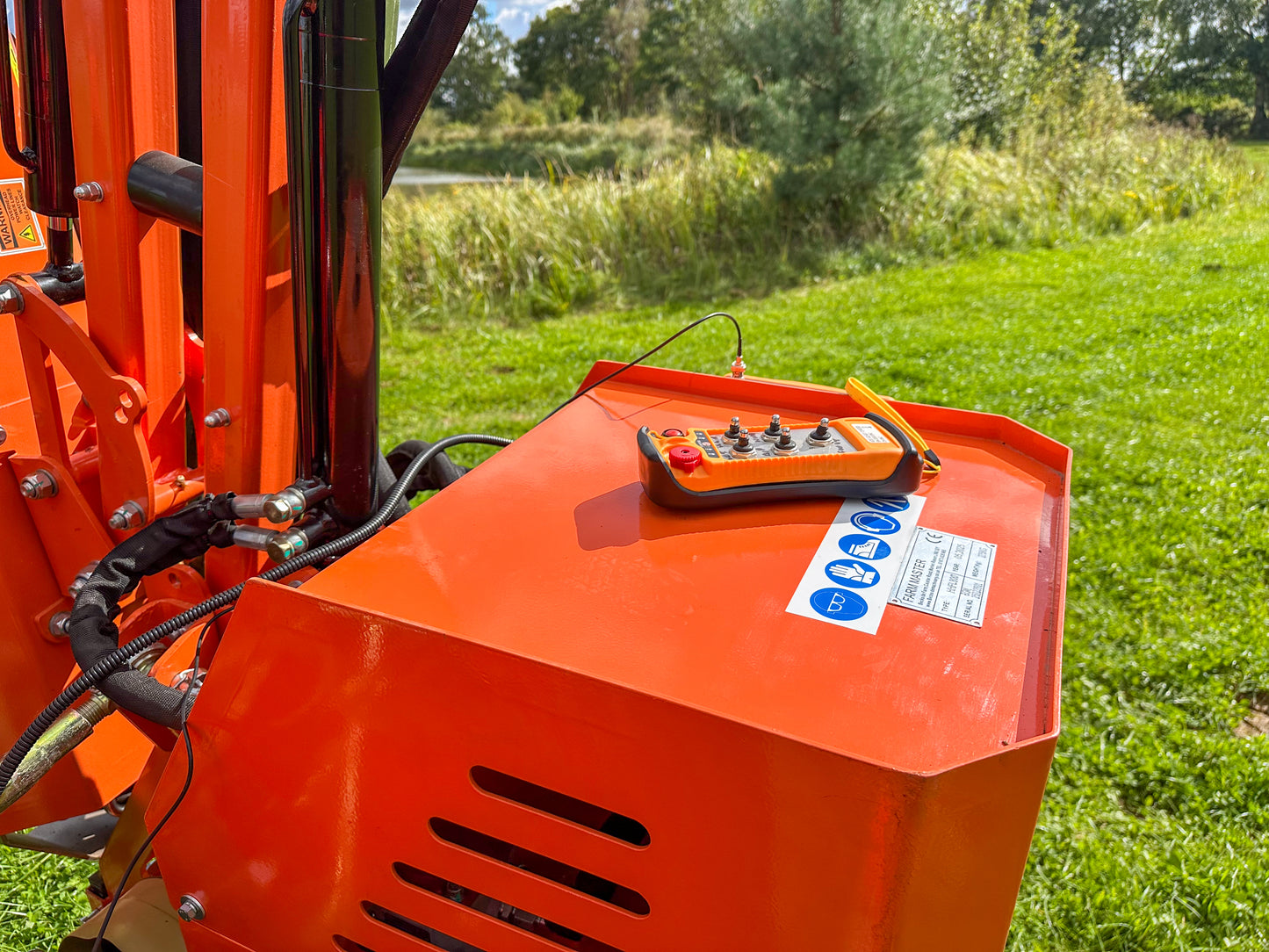 Close-up of a FarmMaster tractor hedge cutter on a grassy field with trees in the background