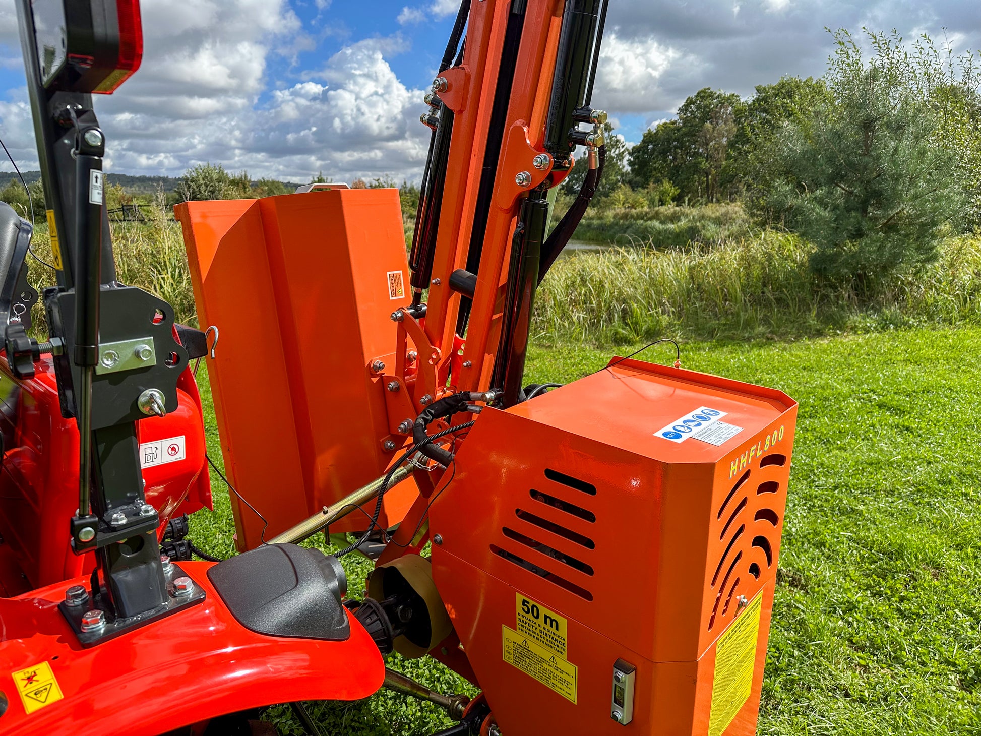 Red tractor with a FarmMaster tractor hedge cutter in a grassy field