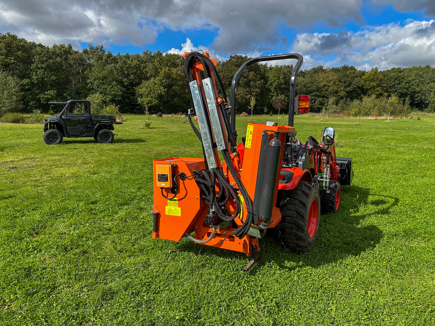 FarmMaster tractor hedge cutter on a grassy field with a forest in the background