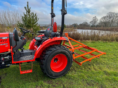 Red tractor with a FarmMaster tractor leveller on a grassy field with a lake and trees in the background.