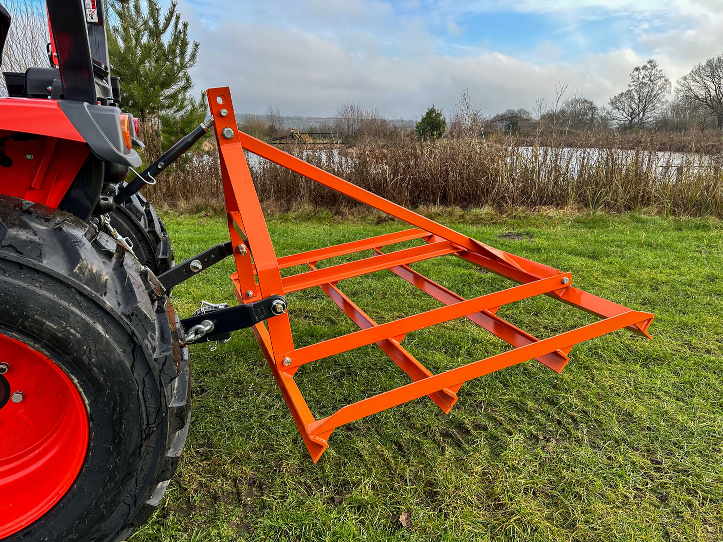 FarmMaster tractor leveller attached to a red tractor on a grassy field.