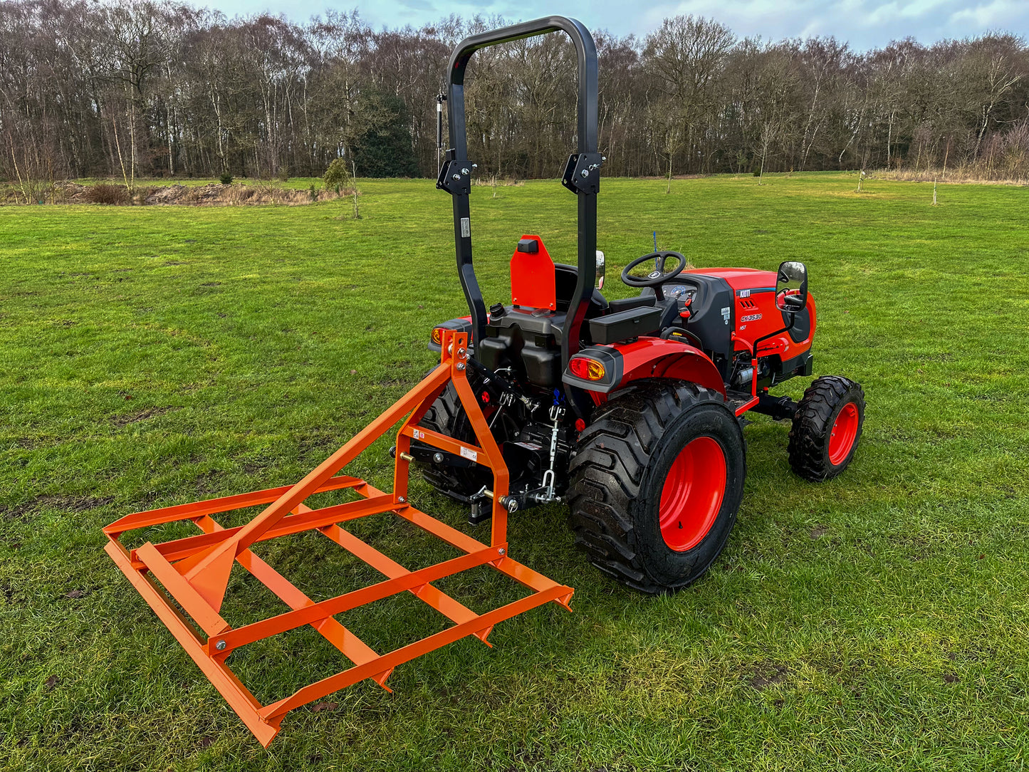 Red tractor with a FarmMaster tractor leveller on a grassy field.