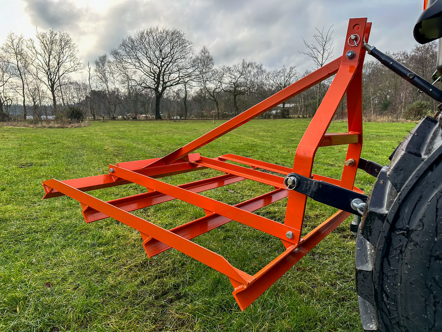 FarmMaster tractor leveller on a tractor in a field with trees and sky in the background