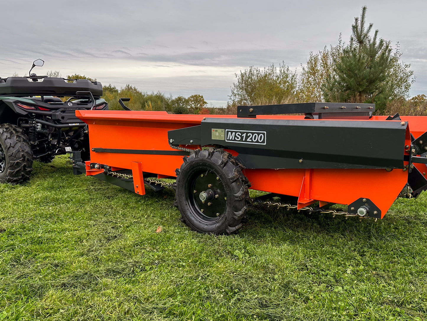 FarmMaster muck spreader on a grassy field with an ATV in the background.