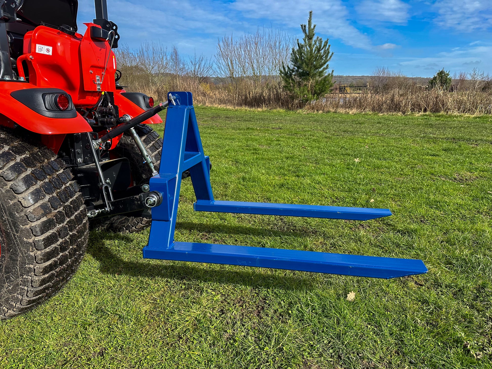 Kioti tractor with a FarmMaster tractor pallet forks in a grassy field with a clear sky.