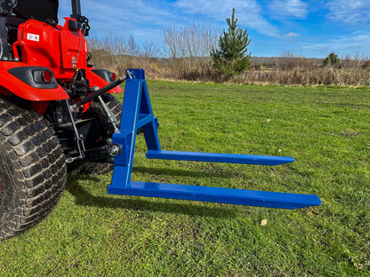Kioti tractor with a FarmMaster tractor pallet forks in a grassy field with a clear sky.