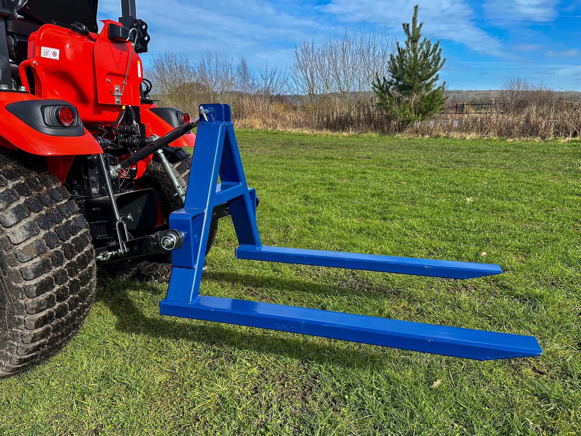 Kioti tractor with a FarmMaster tractor pallet forks attachment on a grassy field.