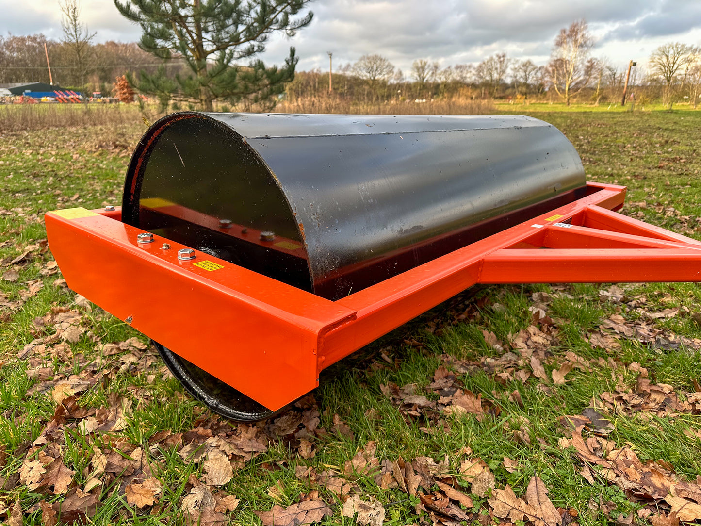FarmMaster tractor land roller on a field with trees and vehicles in the background