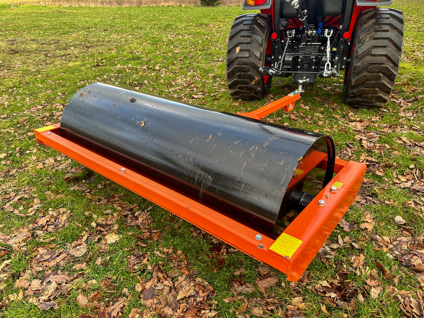 FarmMaster tractor land roller attached to a tractor on a grassy field with leaves.